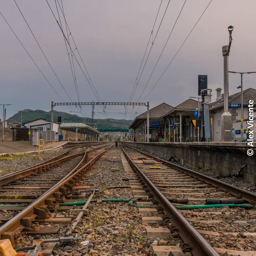 Las vías se extienden hacia las montañas desde una estación tranquila, invitando al viaje interior y exterior.