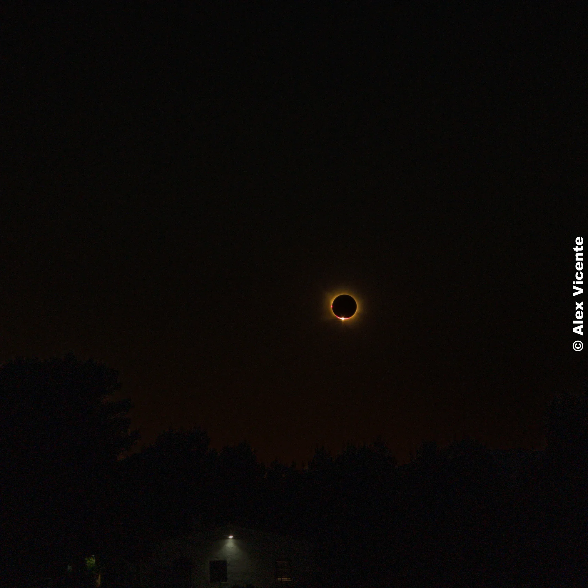 Total solar eclipse over a darkened landscape, a ring of light around the Moon