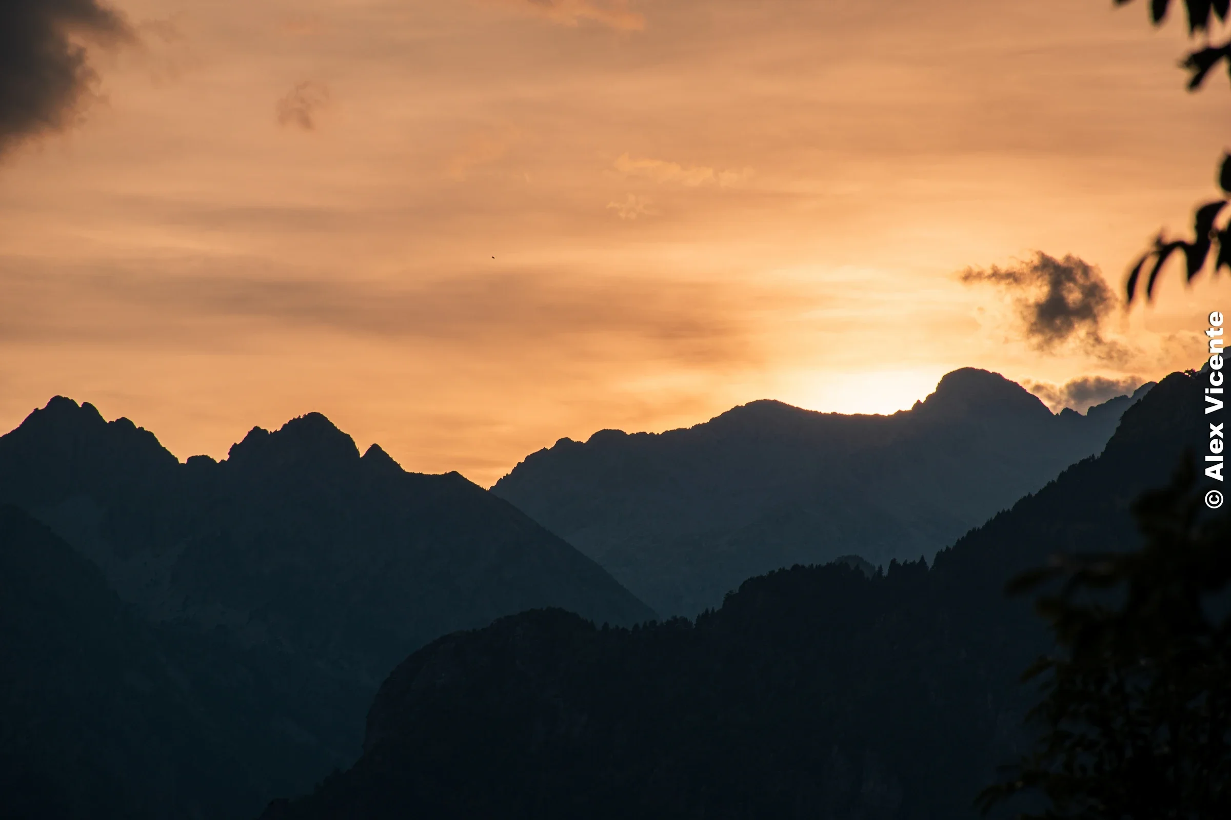 Mountain peaks silhouetted against an orange sunset sky.