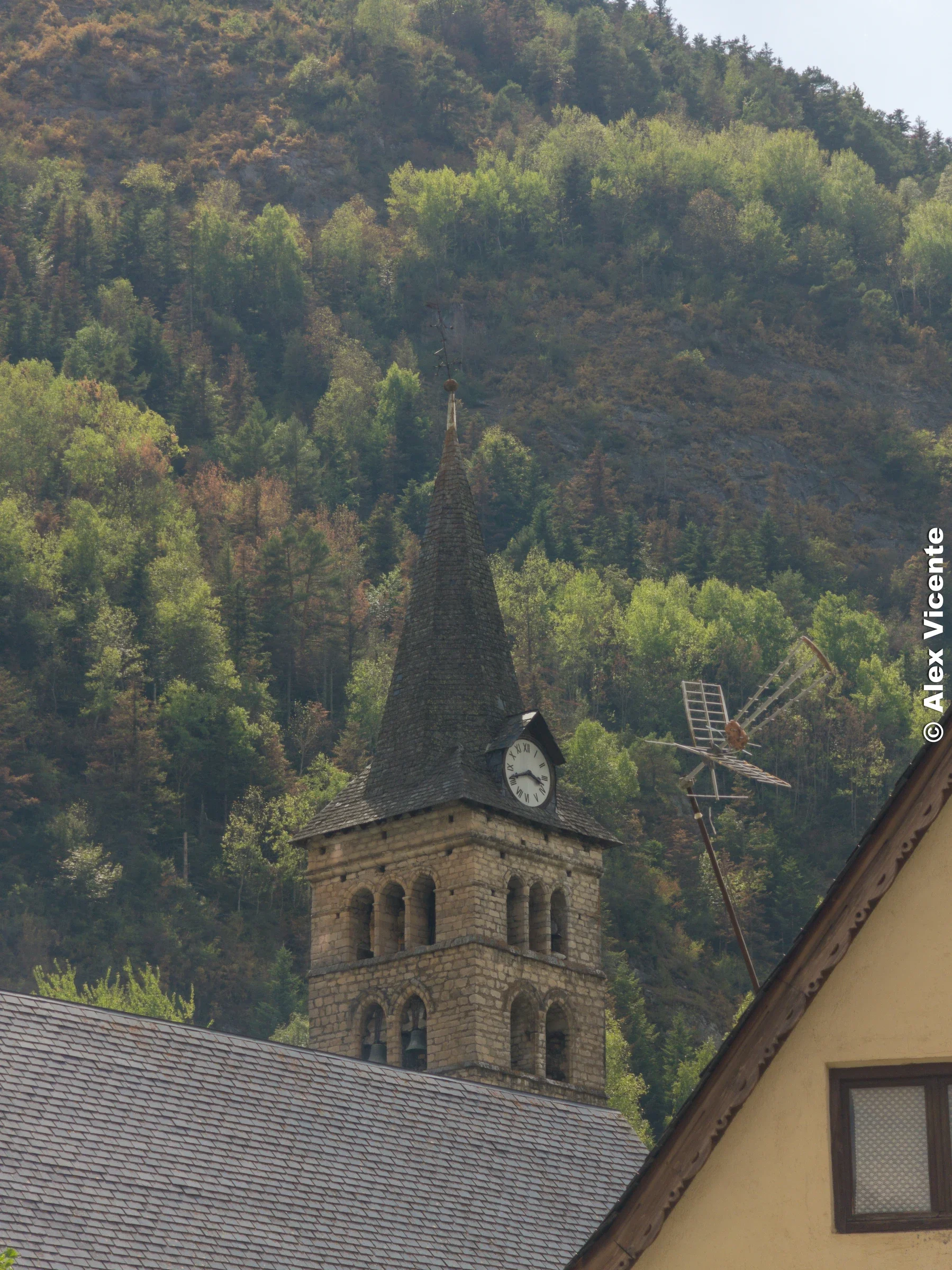 El campanario de piedra asciende hacia un reloj recortado por la luz y las nubes.