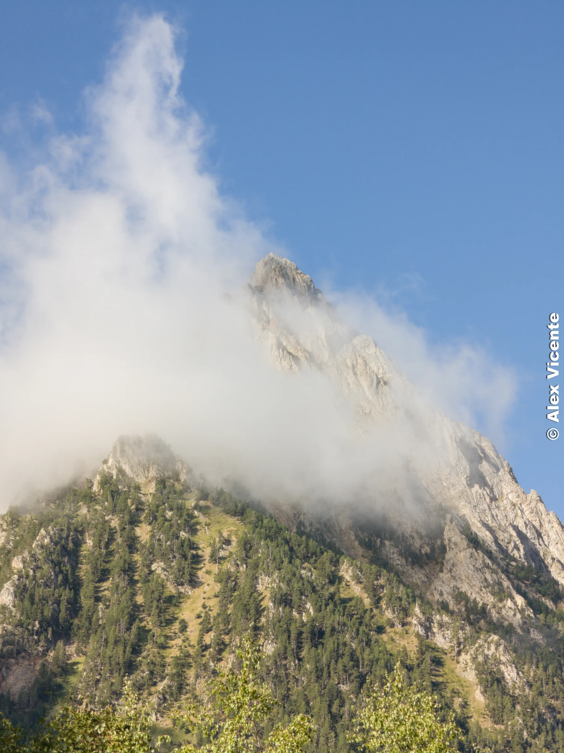 La niebla se abre por un instante y deja ver la arista de la montaña contra el cielo azul.
